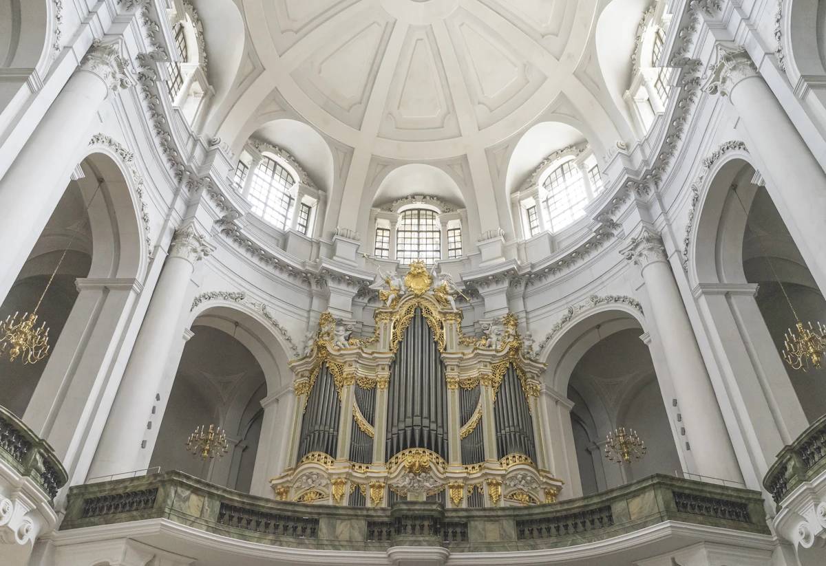 Una cantoria d'organo barocca di chiesa, riccamente decorata in bianco e oro, sotto un soffitto a cupola (immagine rappresentativa di un organo di chiesa barocco — non gli autentici interni gotici in mattoni rossi di St. Jacobi ad Amburgo)