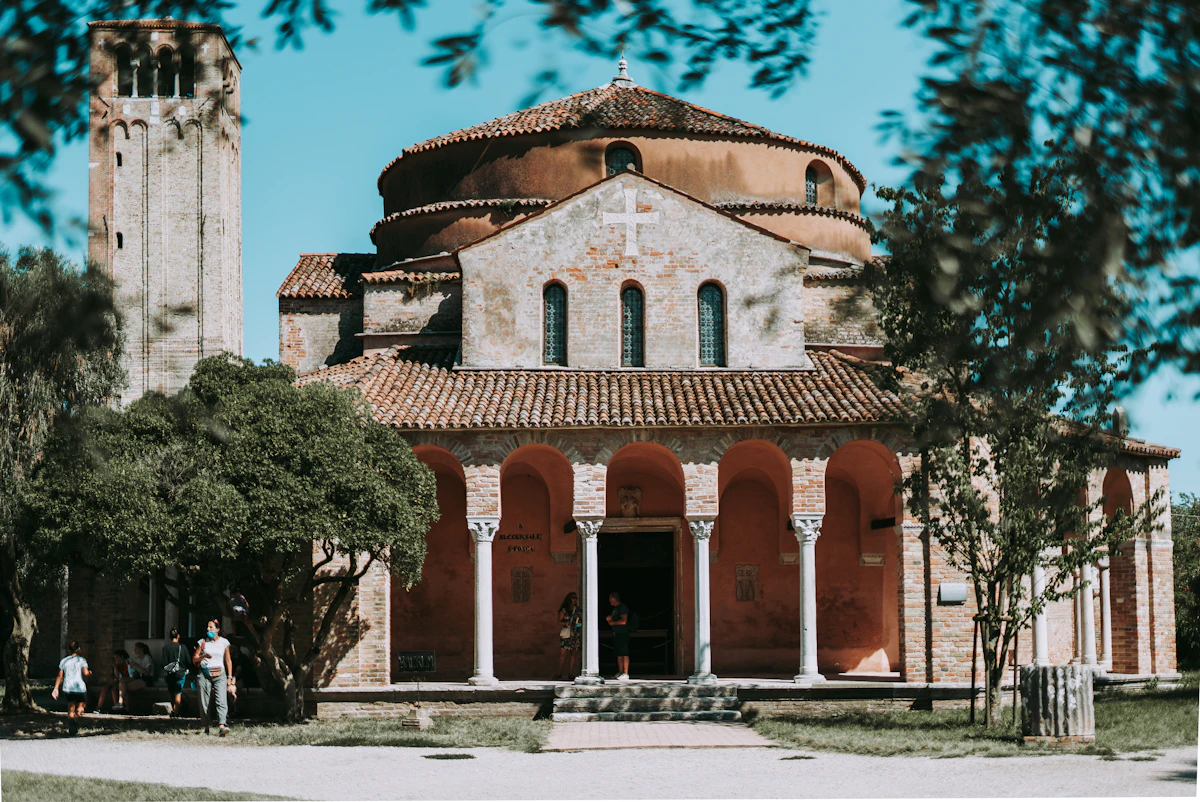 L'abside byzantine en brique de la Basilica di Santa Maria Assunta de Torcello, avec son haut campanile se dressant derrière, entourée d'arbres sur l'île de Torcello