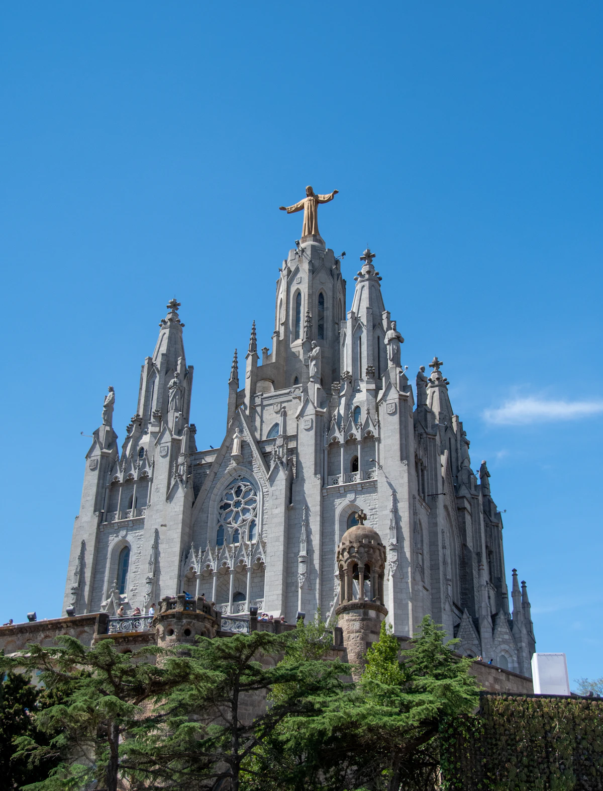 A large building with a statue on top, with Tibidabo mountain and its amusement park visible in the background above Barcelona