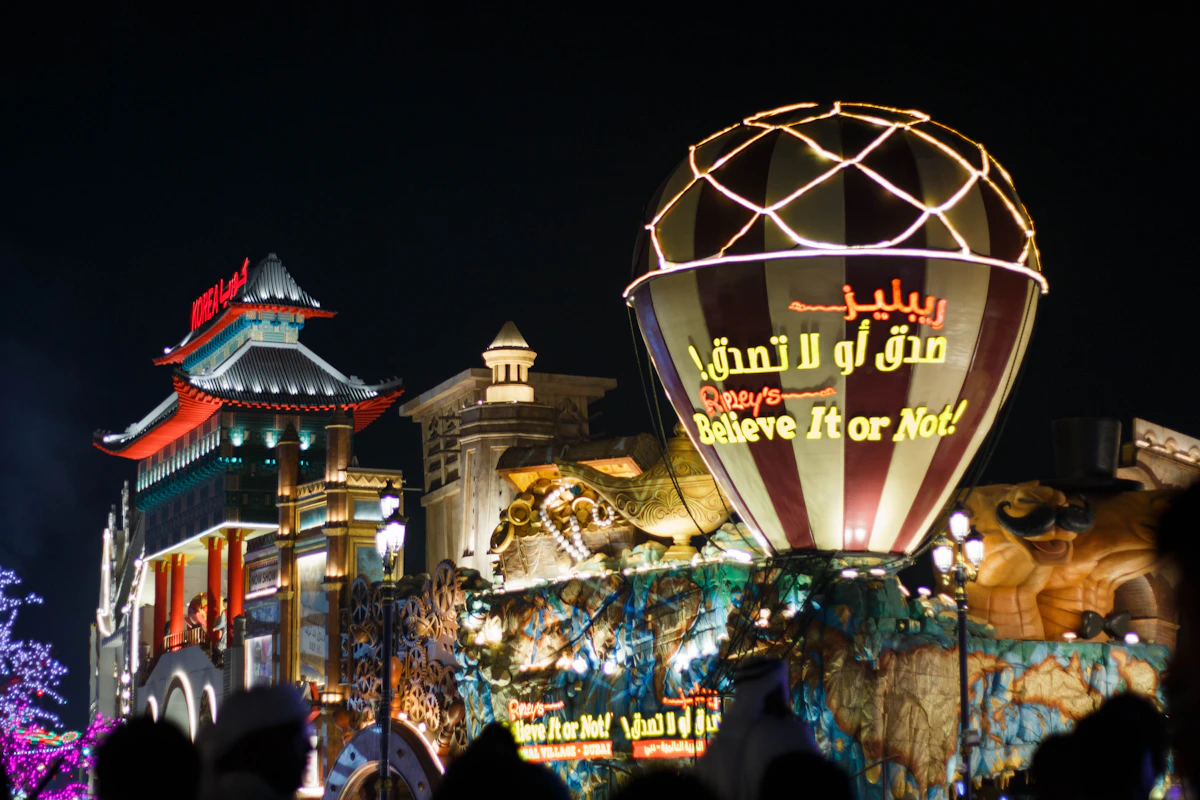 Insegna illuminata di un padiglione e folla a Global Village Dubai di notte
