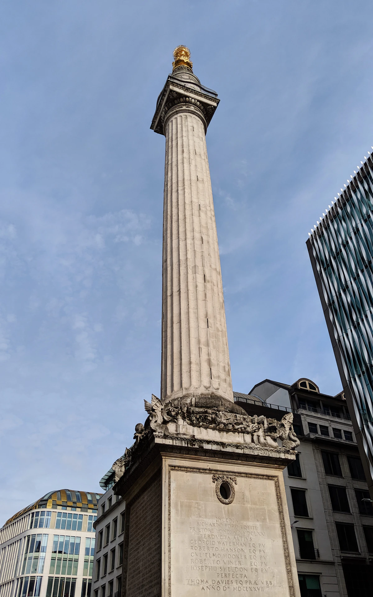 The Monument to the Great Fire of London, una alta columna dórica estriada de piedra coronada por una urna llameante dorada, que se eleva sobre los edificios de la City de Londres
