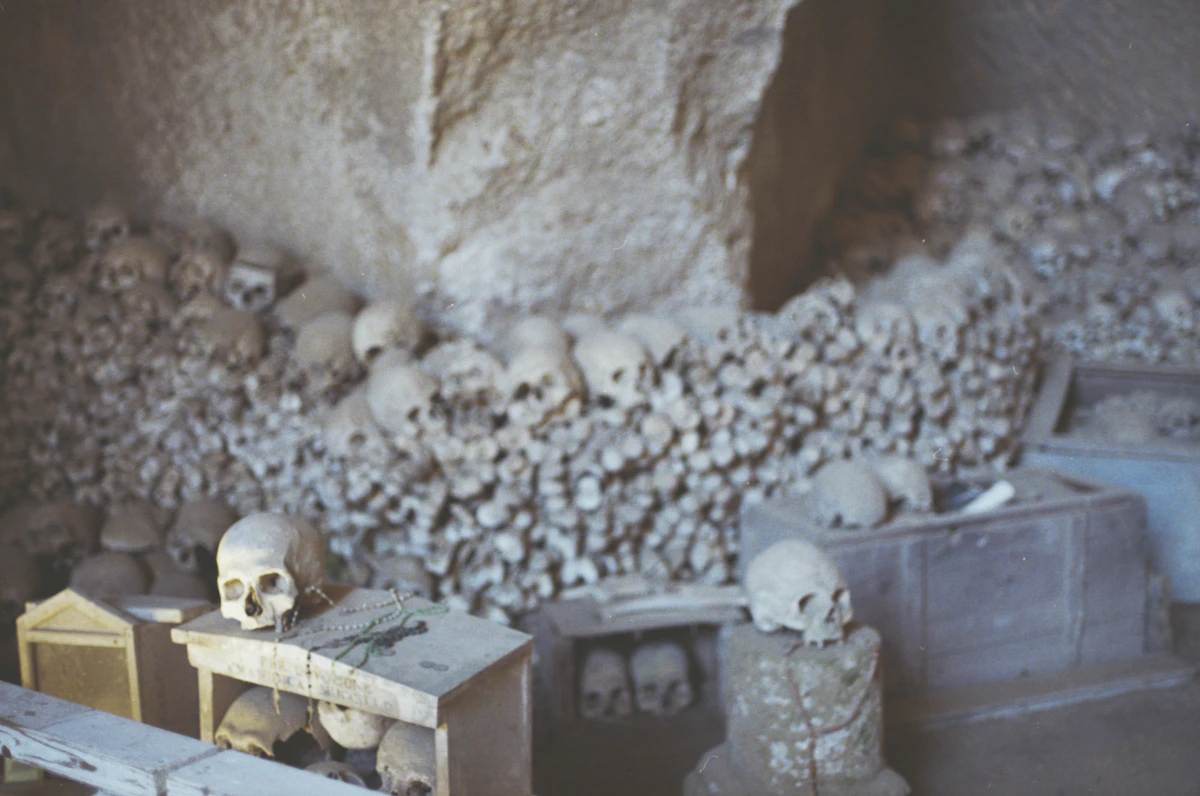 Reihen von Schädeln und Knochen entlang einer Höhlenwand mit kleinen Andachtsschreinen (repräsentatives Bild eines Beinhauses, nicht bestätigt als die eigenen Galerien des Cimitero delle Fontanelle)