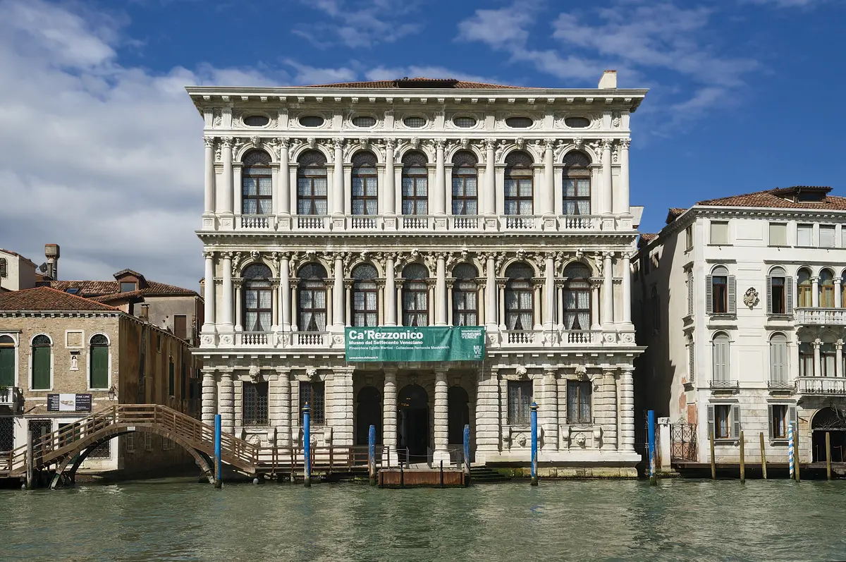 La facciata barocca in marmo bianco di Ca' Rezzonico sul Canal Grande a Venezia, con tre ordini di finestre ad arco e uno striscione del museo 'Ca' Rezzonico' sopra l'ingresso